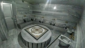Bathroom features a central sink with decorative tile inlay, two toilets with bidet attachments, and a large mirror.