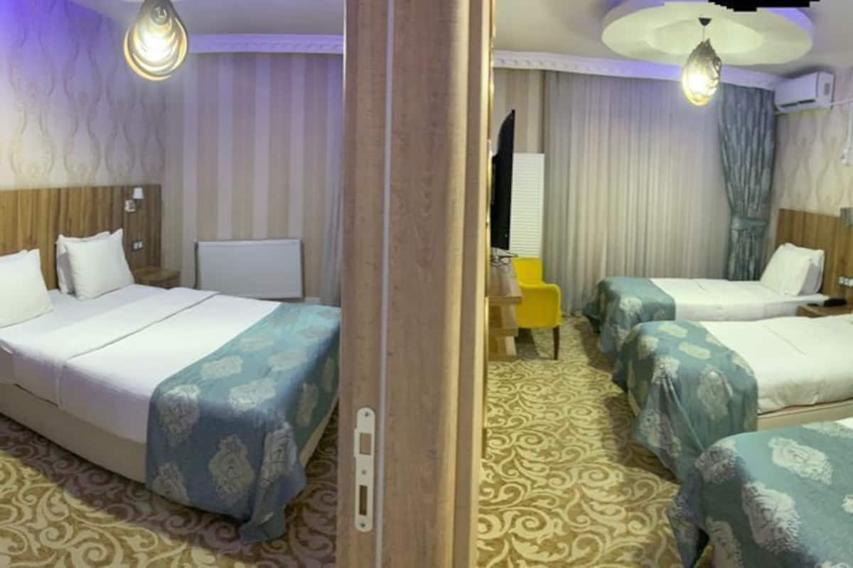 A hotel room with four beds, a wooden headboard, a small desk, and a chair.
