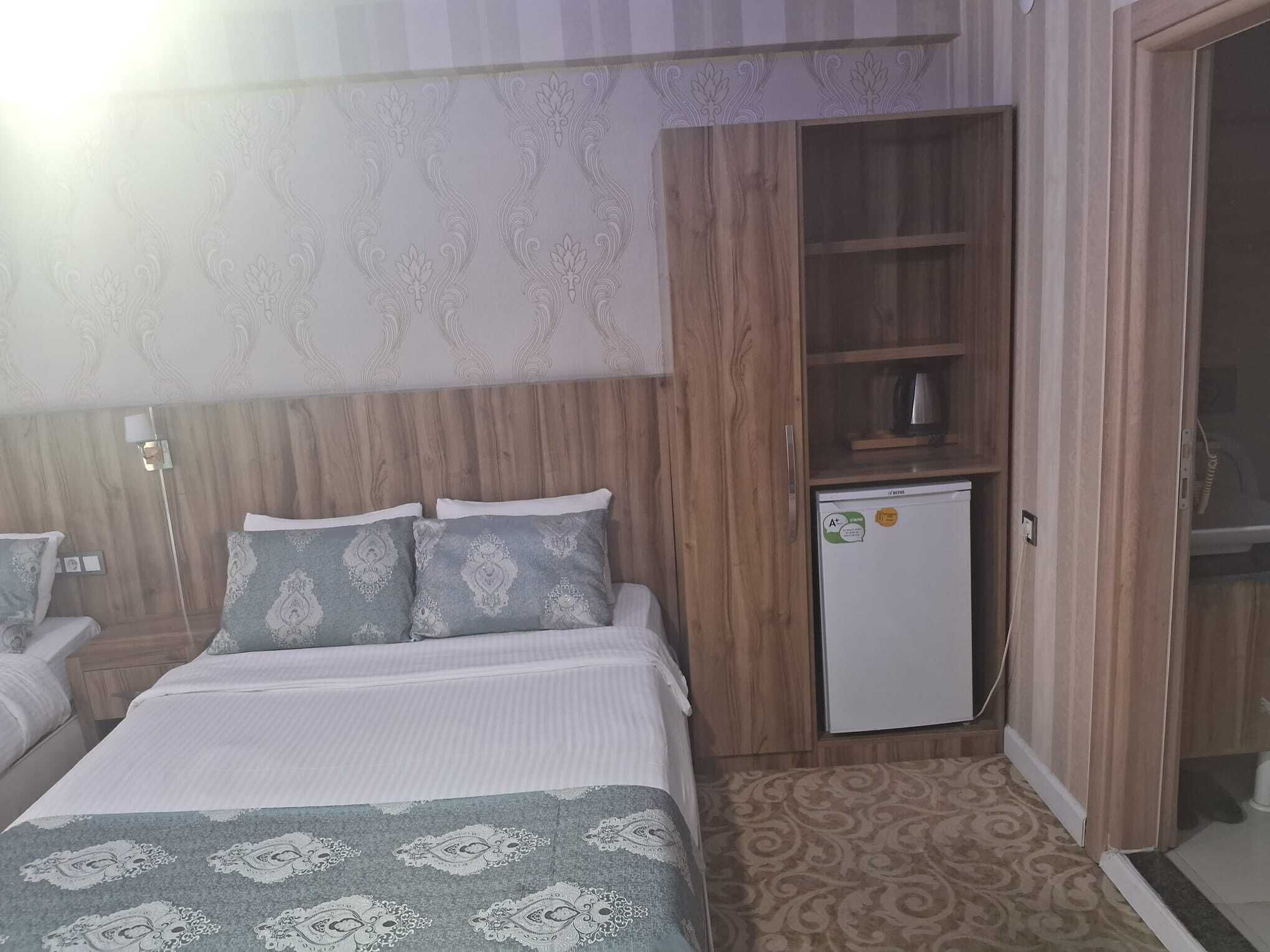 A bedroom with a bed, a wardrobe, a small fridge, and a patterned carpet.