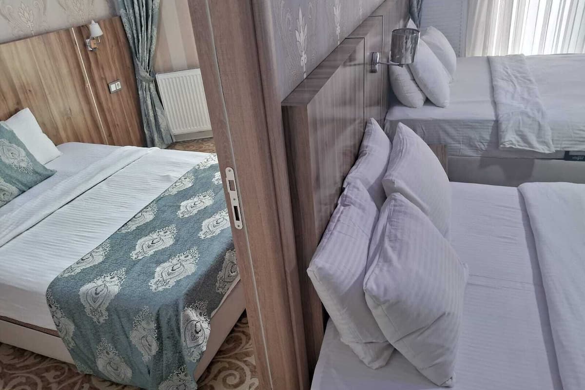A hotel room with a wooden headboard, a bed with white bedding, a bedside table with a lamp, and a patterned carpet.