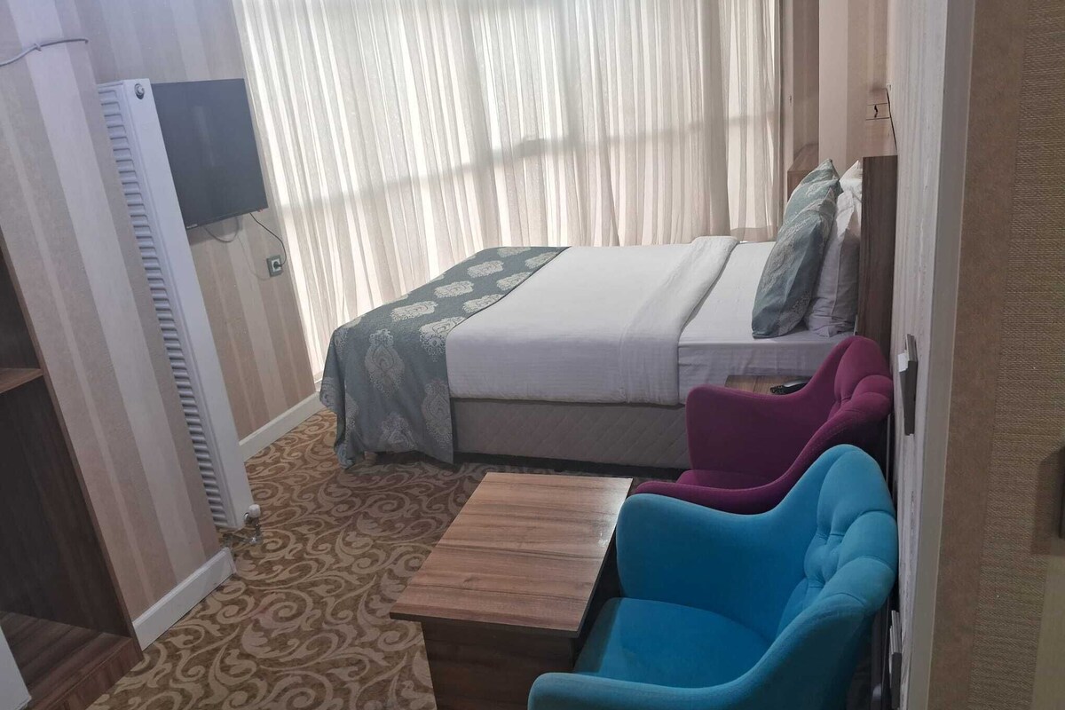 Una habitación de hotel con cama, una mesita, dos sillas y televisión en la pared.