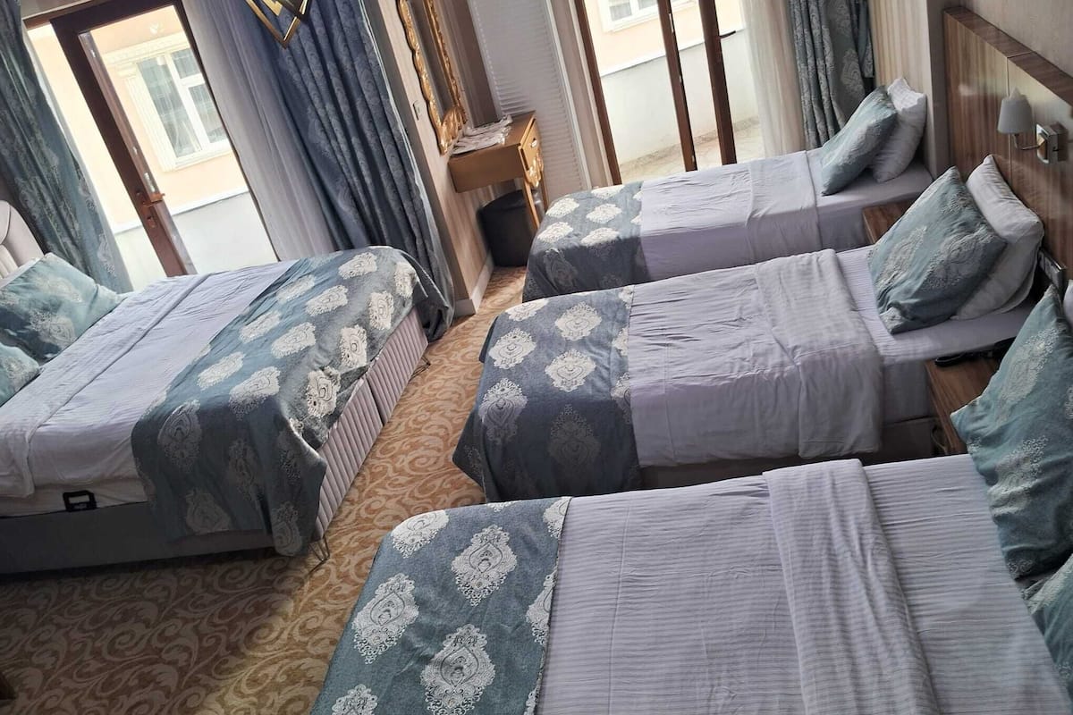 A hotel room with three beds, a wooden floor, and a view of the outside.