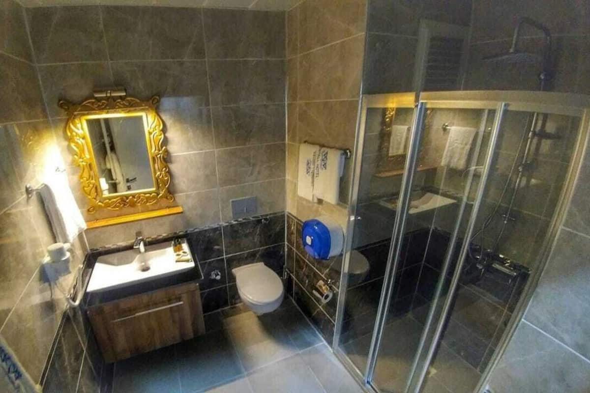 A modern bathroom with a glass shower enclosure, a wooden vanity, and a large mirror with a gold frame.