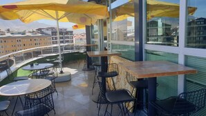 An outdoor seating area with tables and chairs, yellow umbrellas, and a view of buildings in the background. - Crystall Hotel (Van)