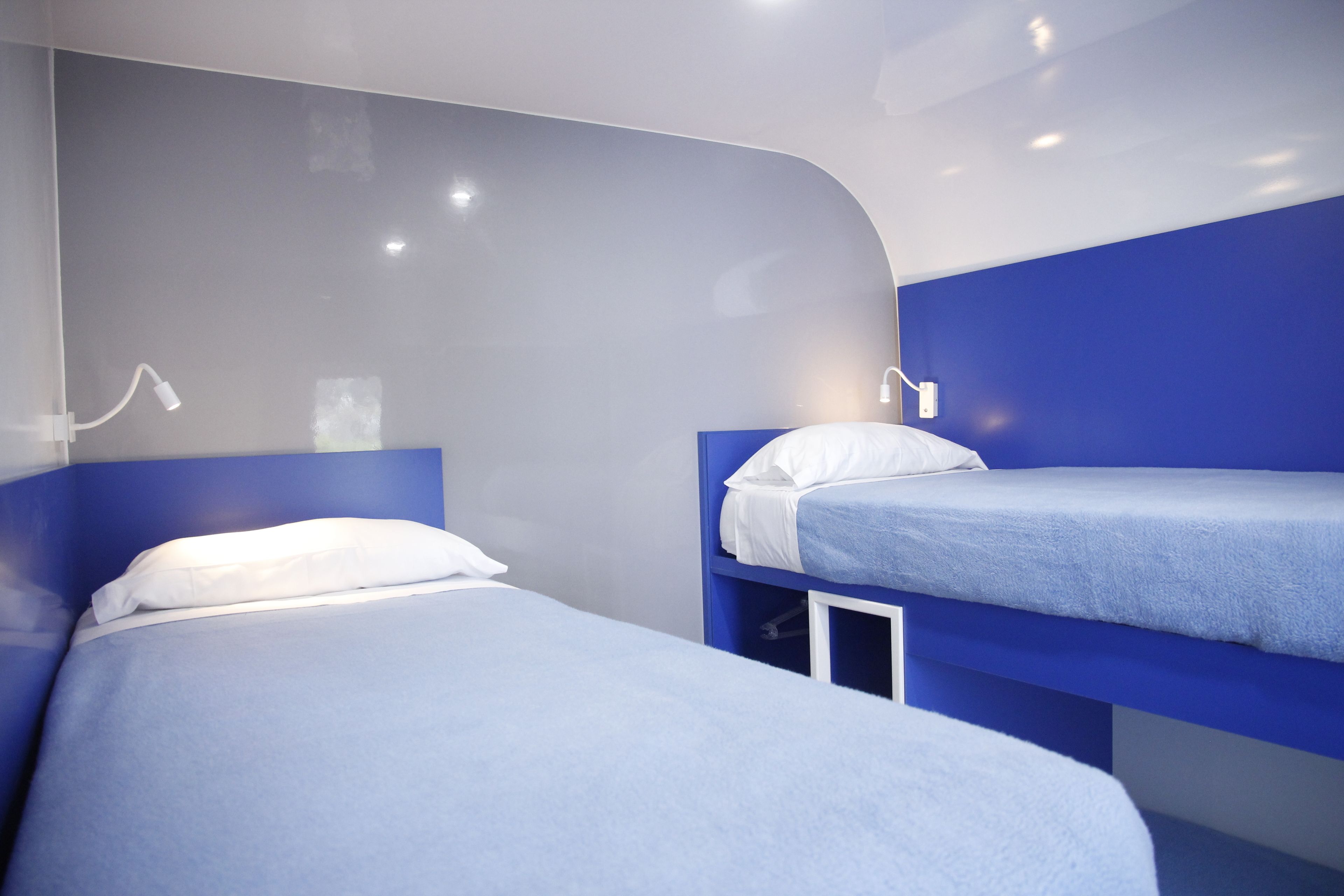 A modern hotel room with two beds, one on the left and one on the right, both with blue headboards and white bedding.
