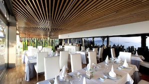 Un restaurante con mesas dispuestas para comer, con un techo moderno de madera y amplios ventanales con vistas panorámicas.