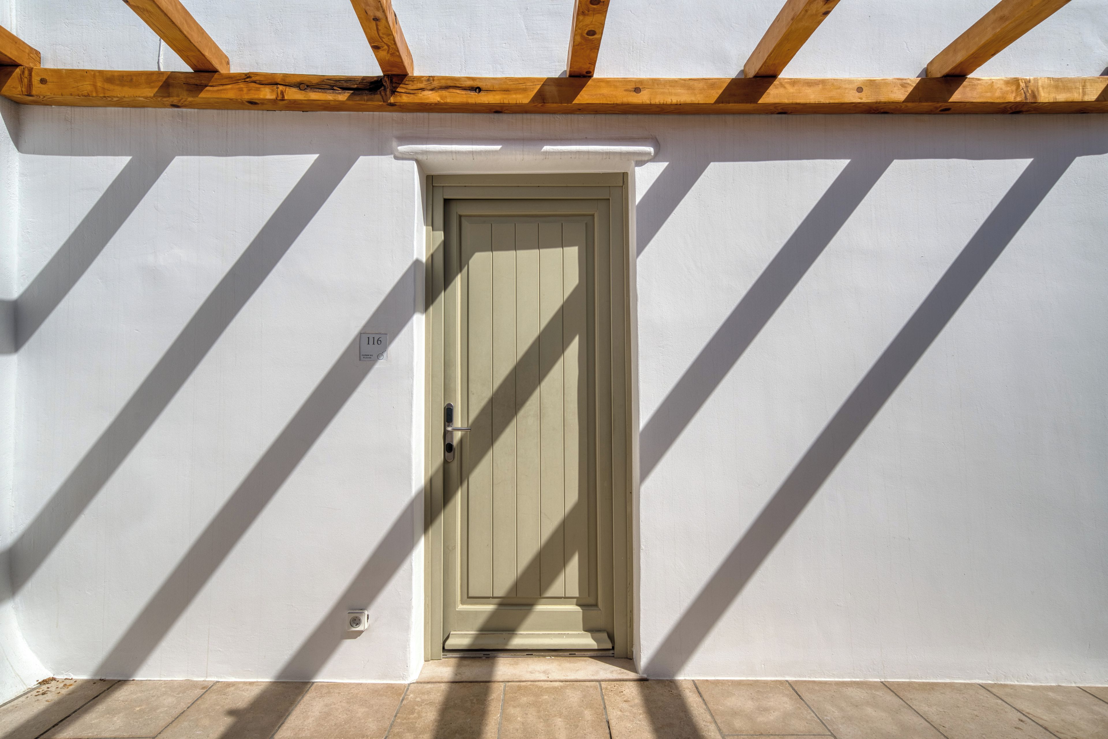 Une porte avec une poignée, une petite fenêtre au-dessus, et une ombre projetée sur le mur.