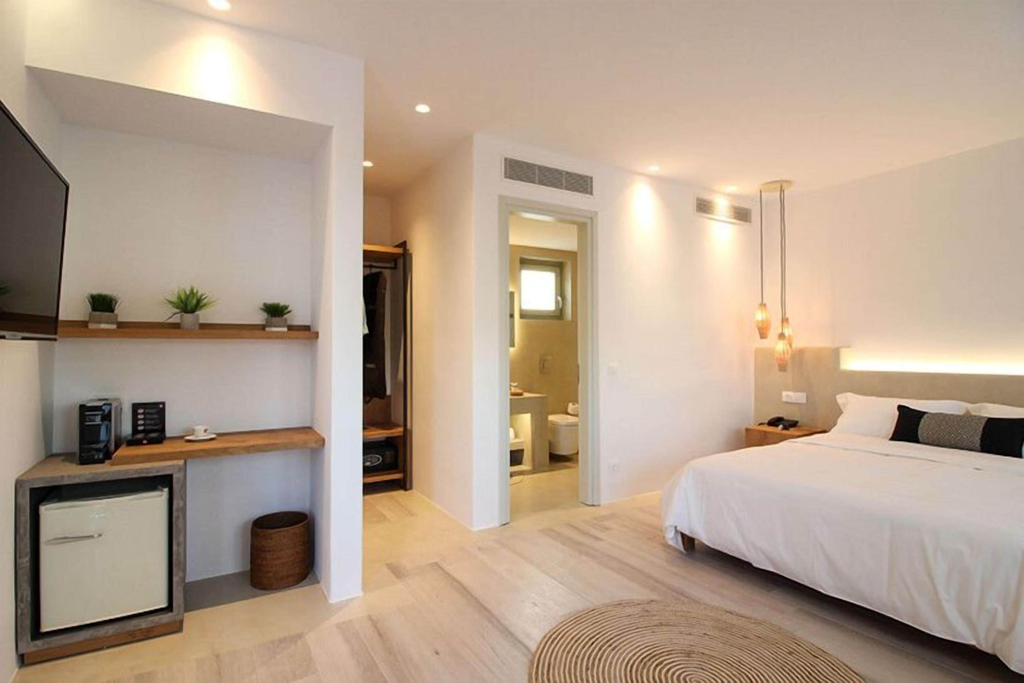 A modern hotel room with a bed, bedside table, TV, and a small desk with a chair.