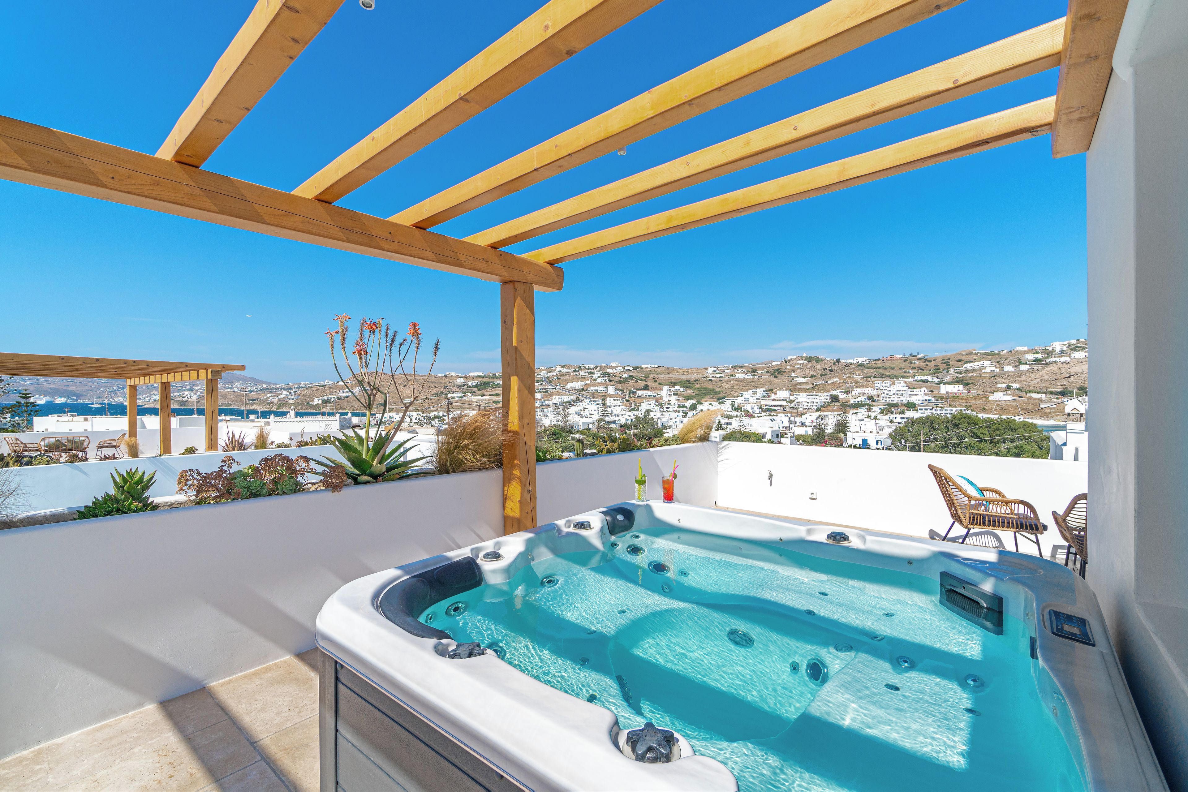 A rooftop terrace with a hot tub, wooden pergola, and a view of a coastal town.