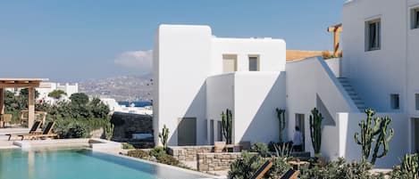 A modern white building with a pool, lounge chairs, and cacti.
