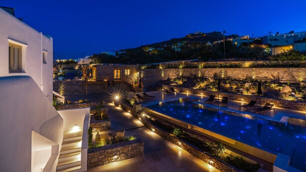 Un área de piscina en la azotea con paredes de piedra, mobiliario exterior y vistas de los edificios circundantes.