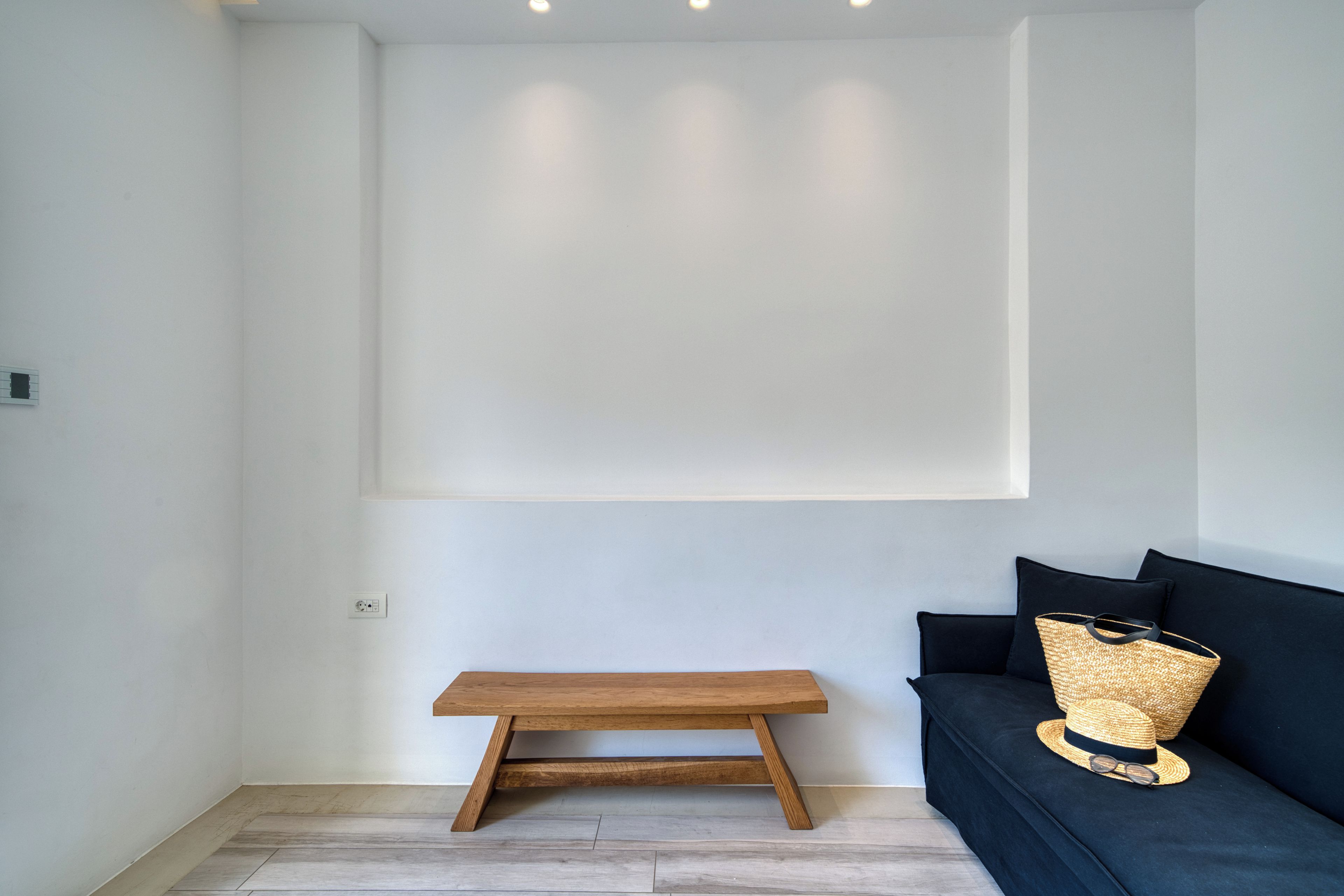A minimalist room with a wooden bench, a dark sofa, and a woven basket on the sofa.