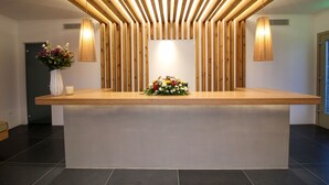 Un mostrador de recepción con techo de listones de madera, un jarrón con flores y una lámpara fijada a la pared.