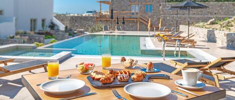 A breakfast setup with a pool view, including a table with plates, cutlery, and a glass of orange juice.