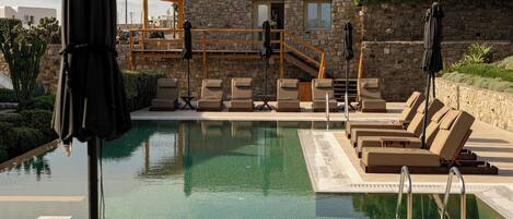 A pool area with lounge chairs and umbrellas, surrounded by stone walls and greenery.