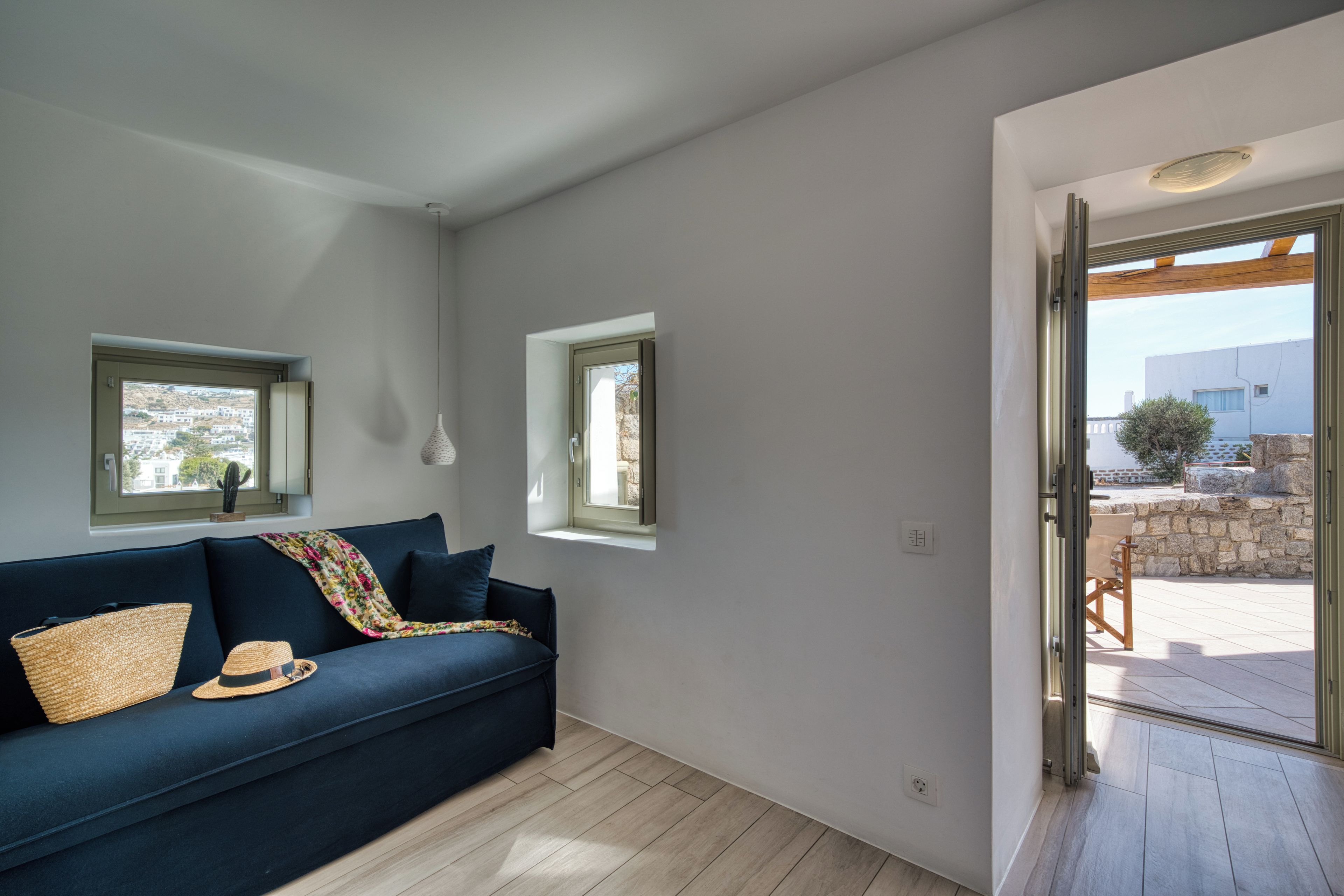 Un salon moderne avec un canapé bleu foncé, deux fenêtres et une vue sur l’extérieur.