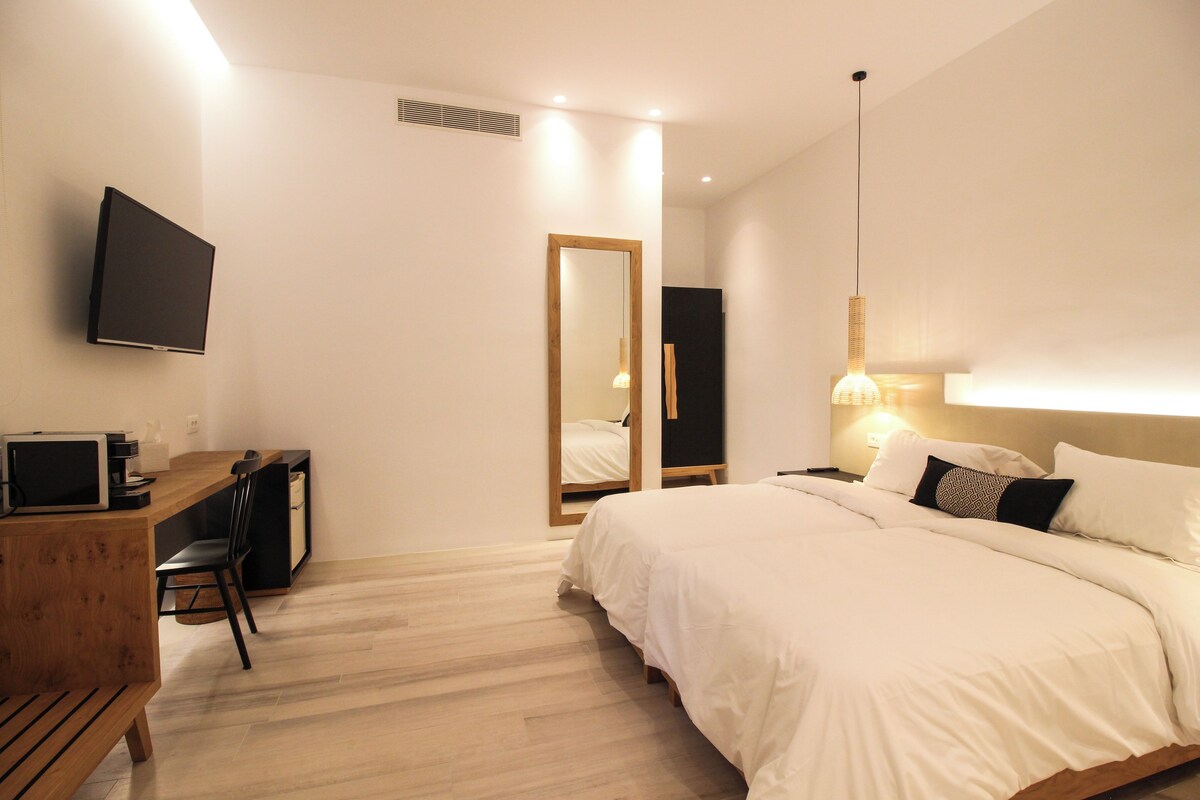 Habitación de hotel con una cama, un escritorio con computadora, un televisor y un espejo.