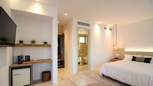Un dormitorio con cama, mesita de noche y escritorio con computadora y plantas.