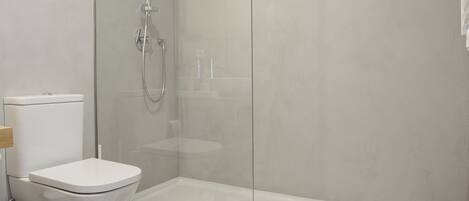 A modern bathroom with a glass-enclosed shower, a toilet, and a patterned floor.