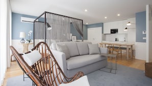 Ein modernes Wohnzimmer mit grauem Sofa, Korbstühlen, einem Essbereich und einer Küche im Hintergrund.