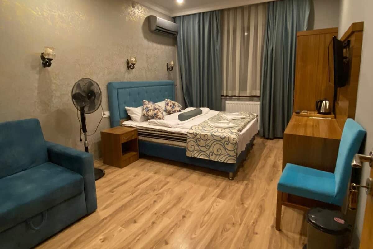A modern bedroom with a bed, a blue sofa, a desk, and a fan.