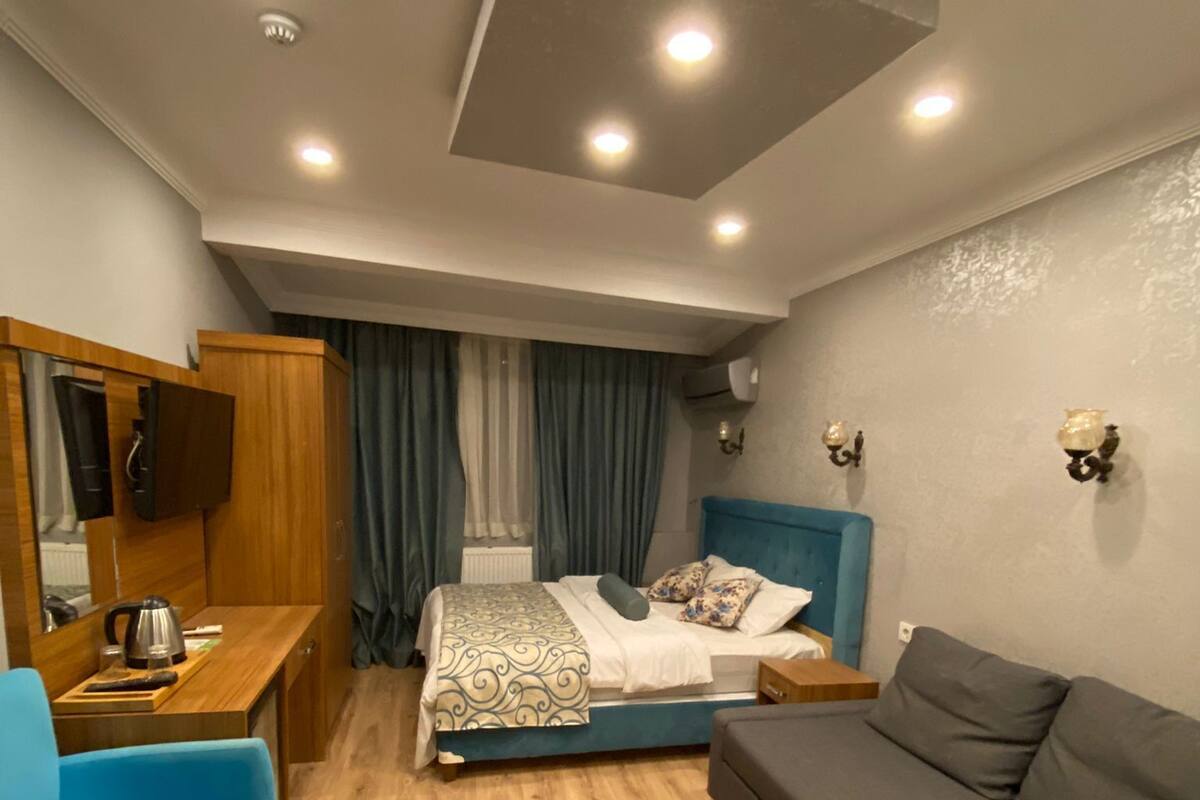 A modern bedroom with a bed, a desk, a blue chair, a grey sofa, and wooden flooring.