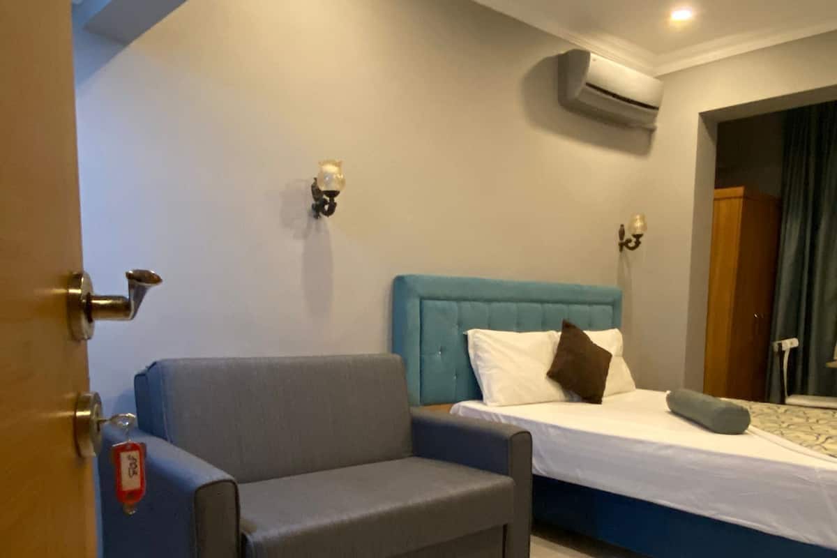 A modern hotel room with a bed, a grey sofa, and a door with a lock.