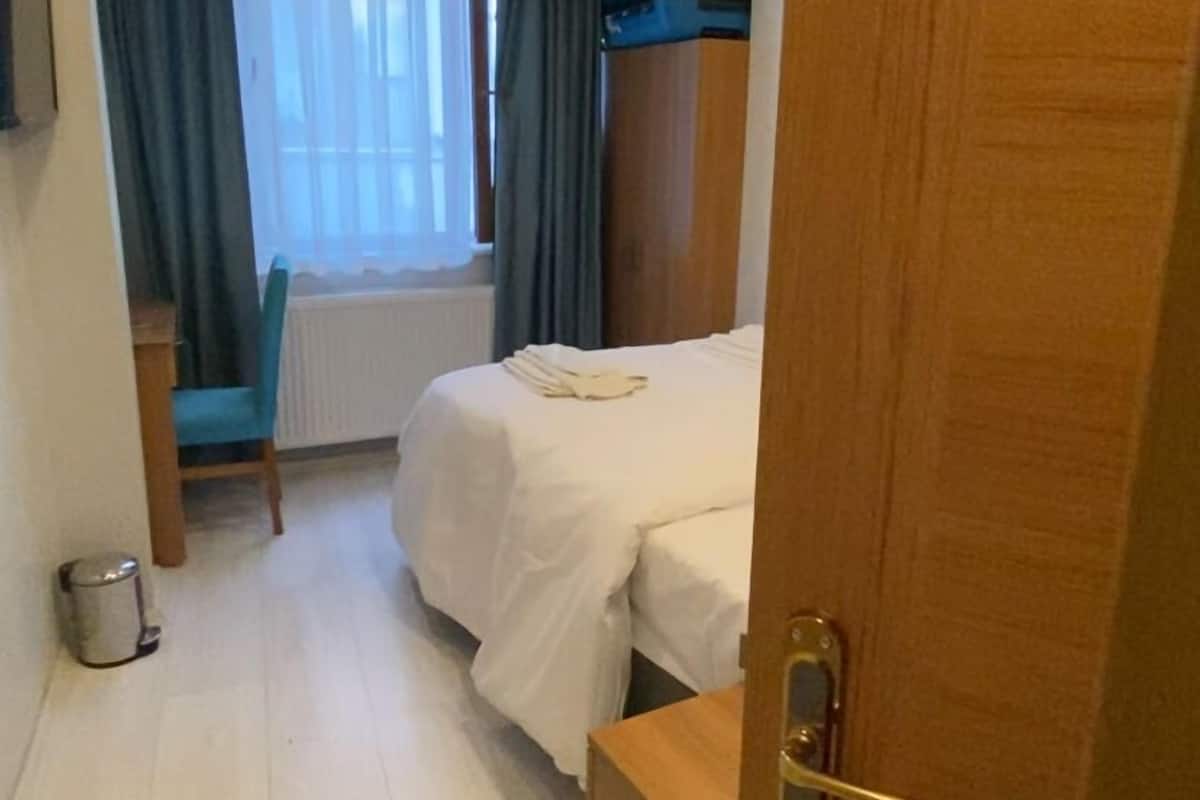 A hotel room with a bed, a desk, a chair, a radiator, and a window with curtains.