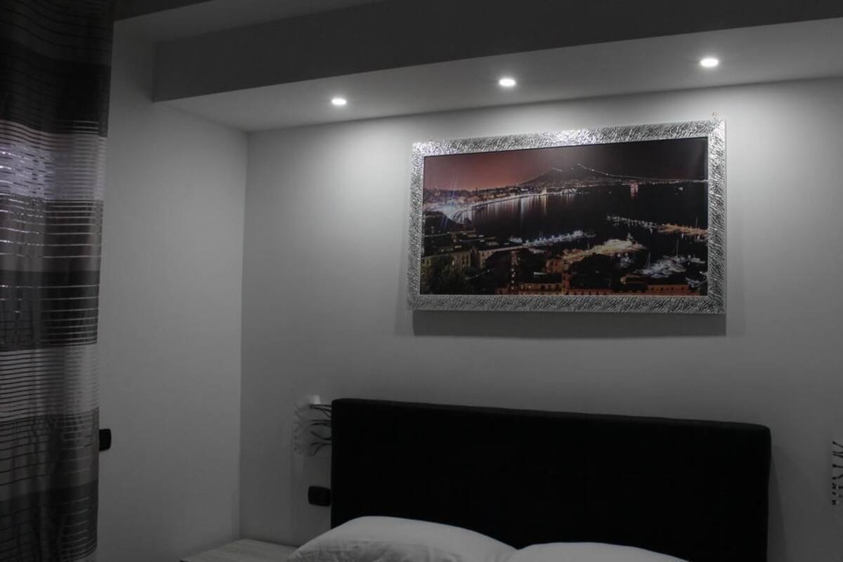 A bedroom with a large bed, a framed picture on the wall, and a window with blinds.