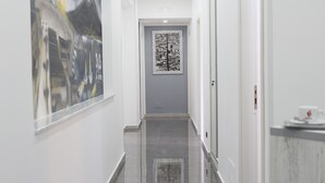 Un couloir avec un sol carrelé, une porte au fond et un tableau encadré au mur.