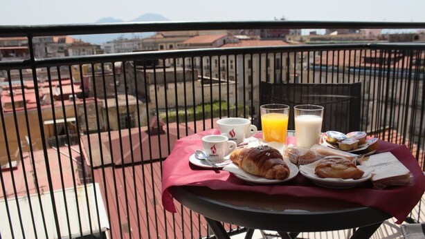 Une table sur le balcon avec un assortiment de produits pour le petit-déjeuner, notamment des croissants, du jus de fruits et du café.