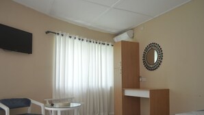 Ein Hotelzimmer mit Bett, Schreibtisch, Stuhl, Fernseher, Spiegel und einem Fenster mit Vorhängen.