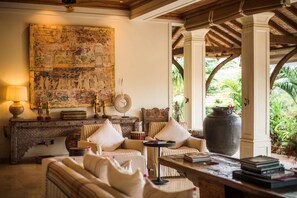 A cozy living area with a sofa, armchairs, a coffee table, and a bookshelf. A large painting adorns the wall, and a large vase is on the floor. - Kahani Paradise (Kumta)