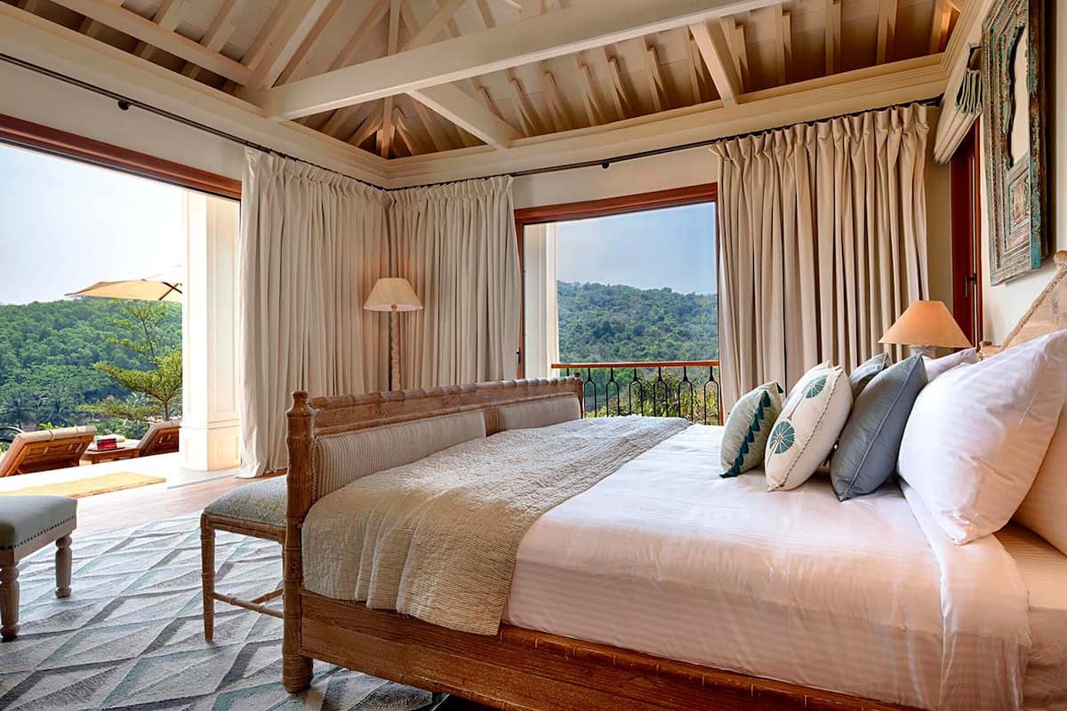 A bedroom with a large bed, a balcony with a view, and a wooden ceiling.