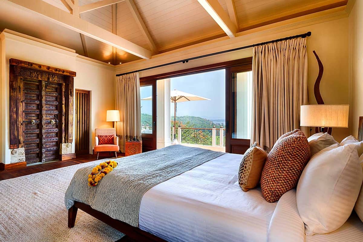 A spacious bedroom with a large bed, a wooden door, a balcony with a view, and a chair.