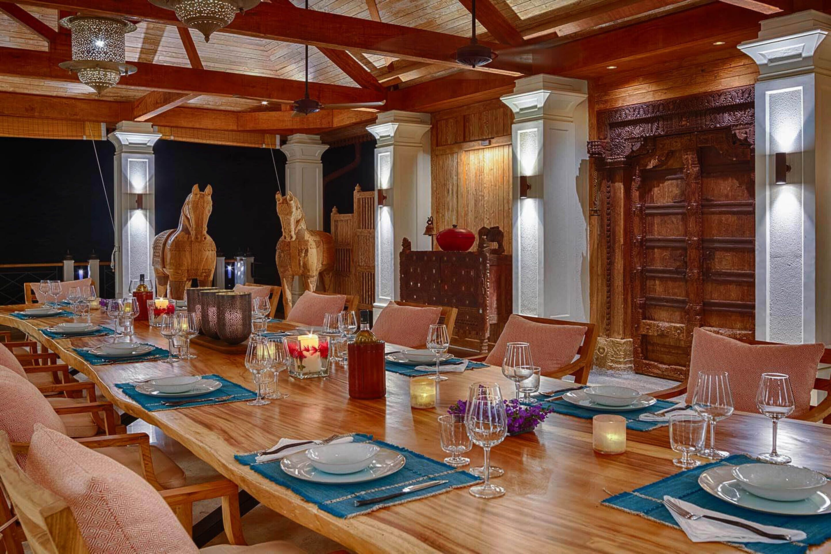 Comedor con una larga mesa de madera dispuesta para una comida, que incluye una araña, velas y adornos.