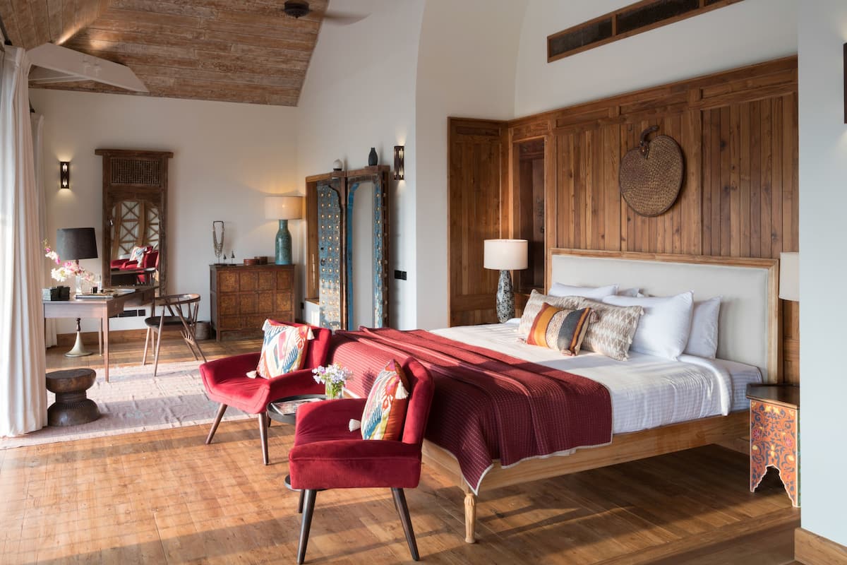 A spacious bedroom with a large bed, wooden headboard, and a red chair.