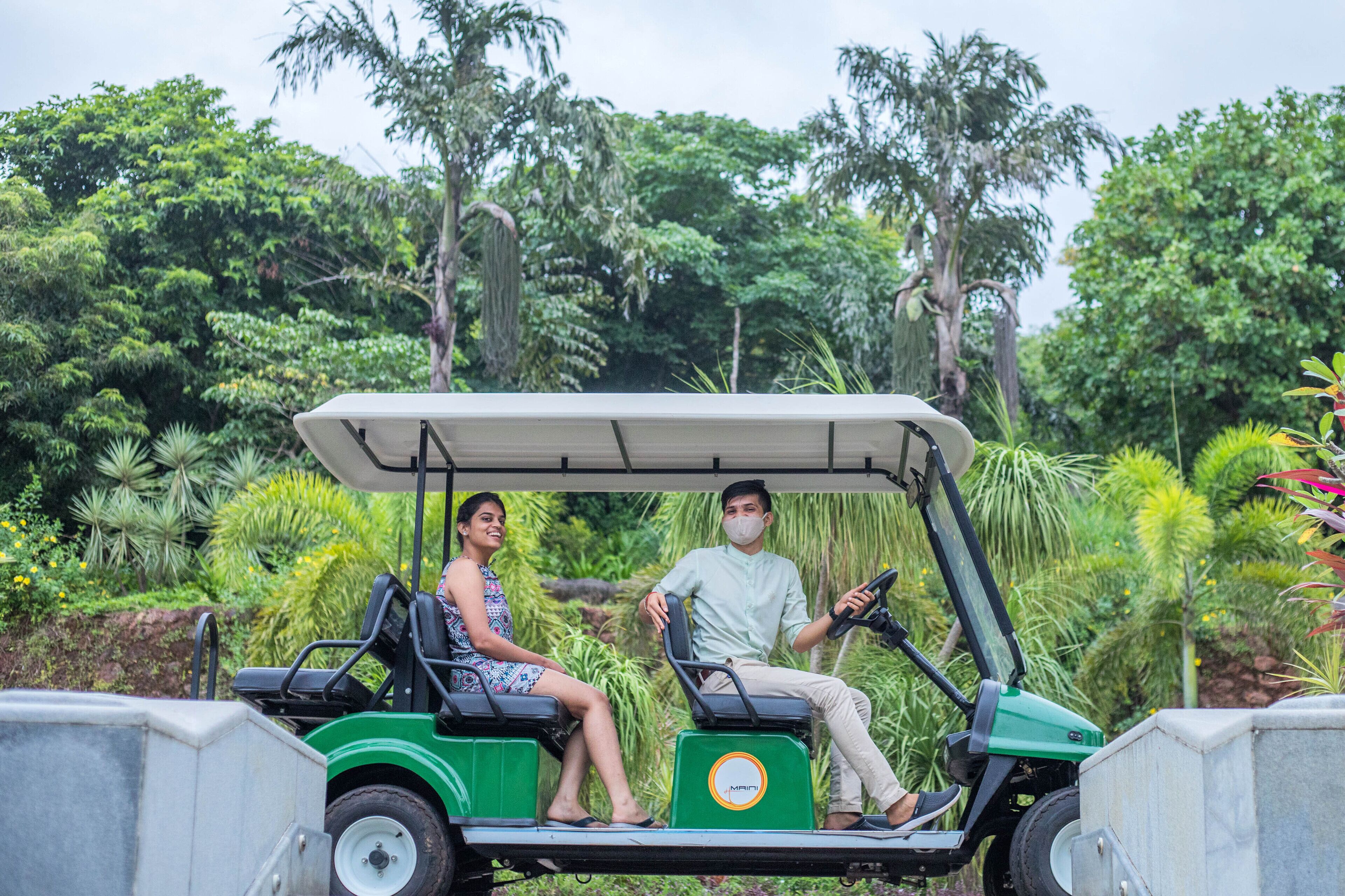 A golf cart with two people, surrounded by lush greenery and trees.