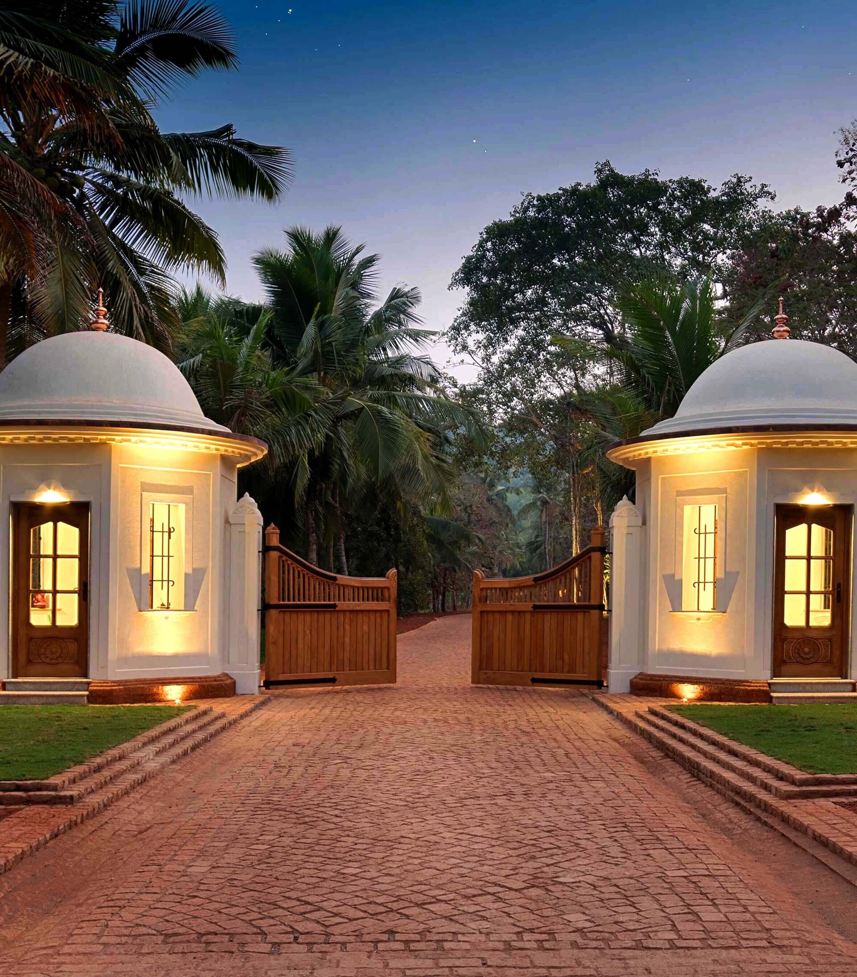A gated entrance with two domed structures, a cobblestone pathway, and tropical vegetation.