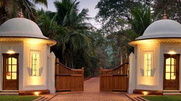A gated entrance with two domed structures, a cobblestone pathway, and tropical vegetation.