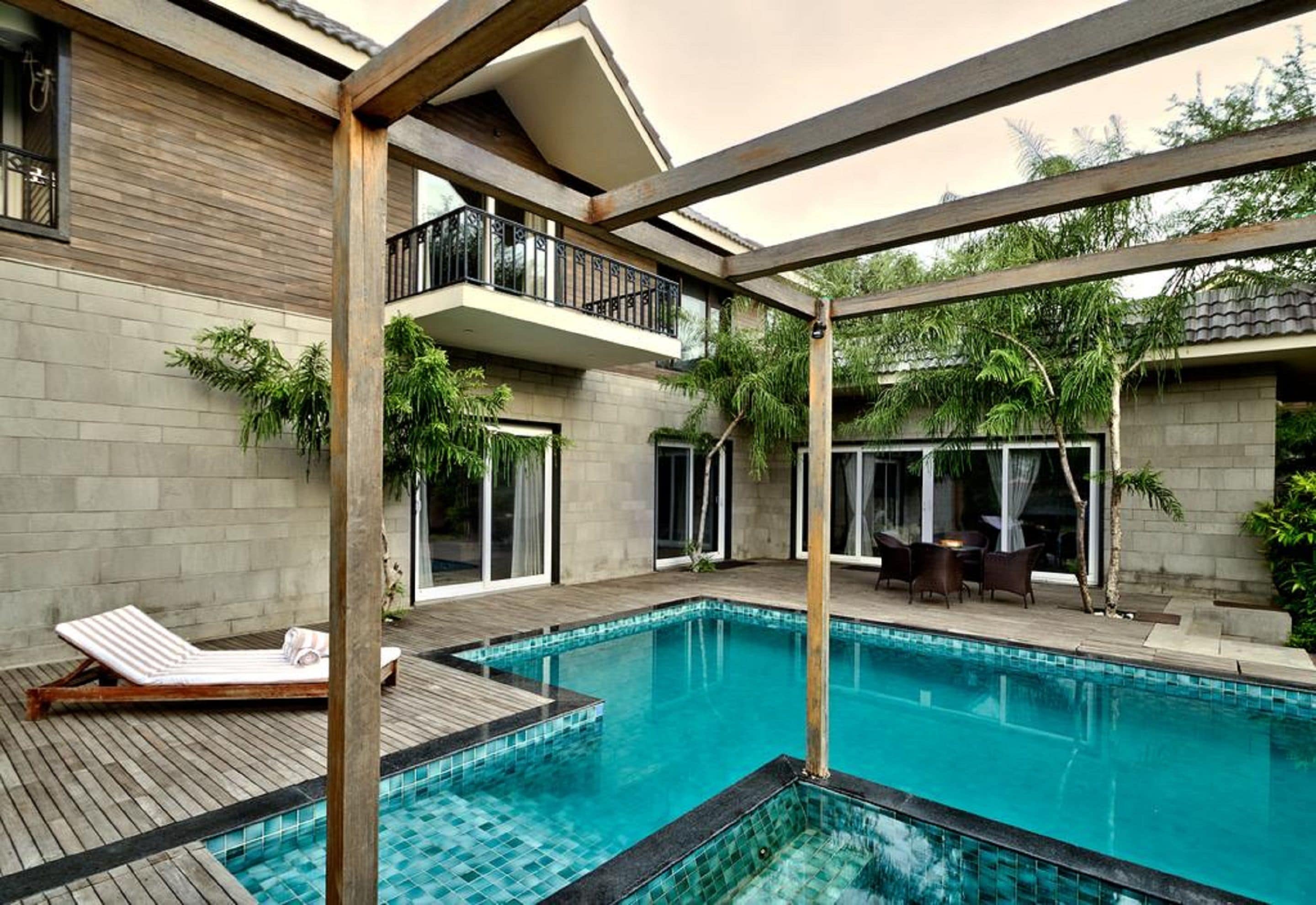 A pool area with a wooden deck, lounge chairs, and a covered seating area with a table and chairs.