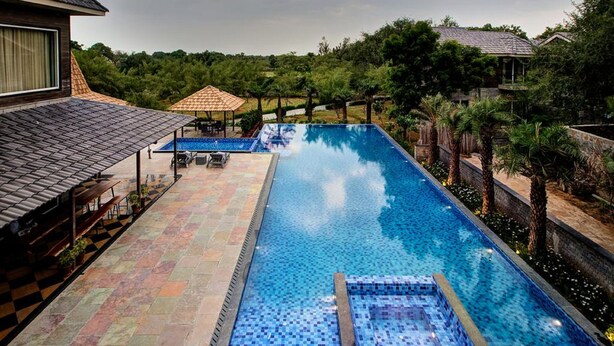 Una piscina rectangular con un área de terraza con baldosas, rodeada de exuberante vegetación y un pabellón.