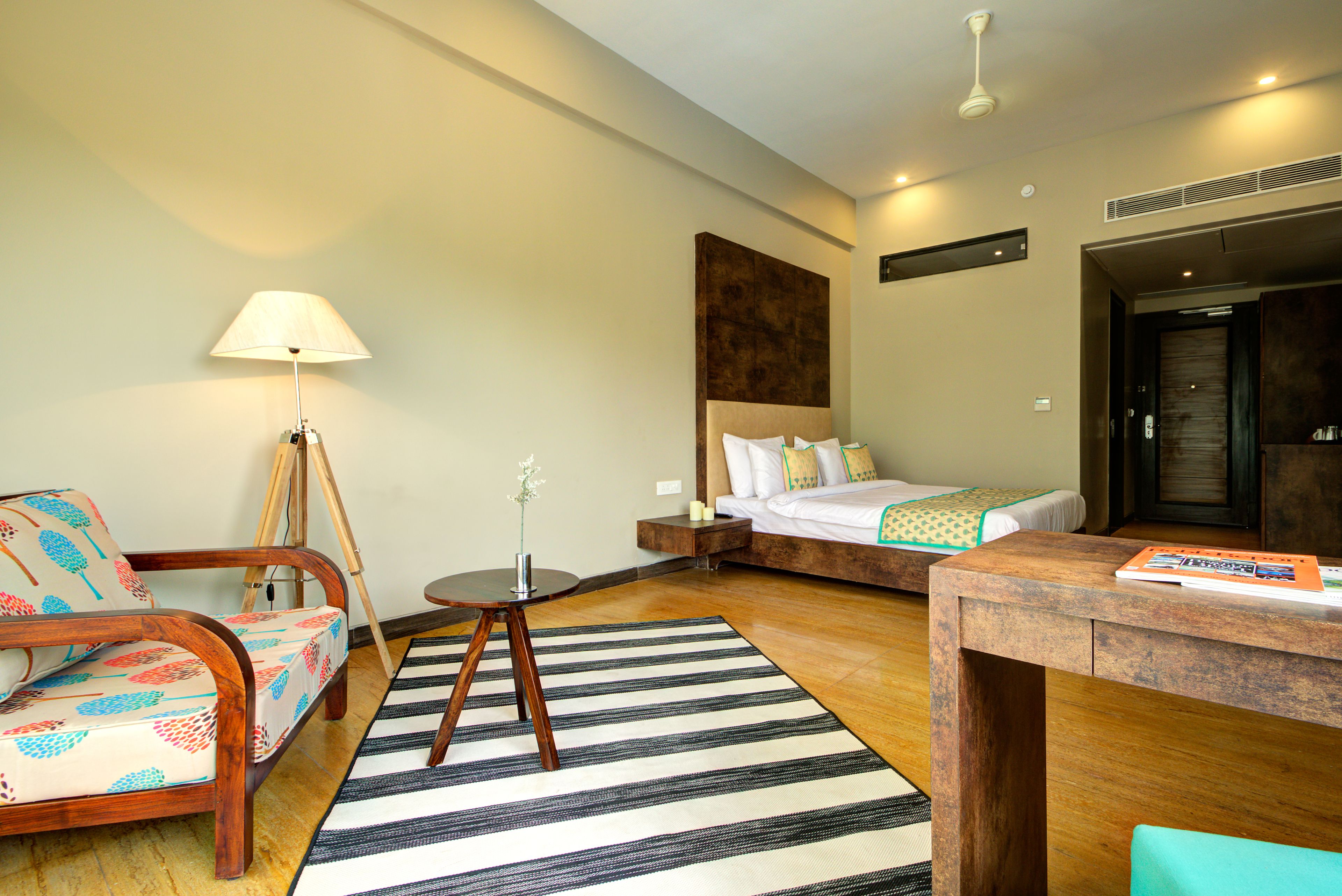 A hotel room with a bed, a wooden chair, a small table, a lamp, and a striped rug.