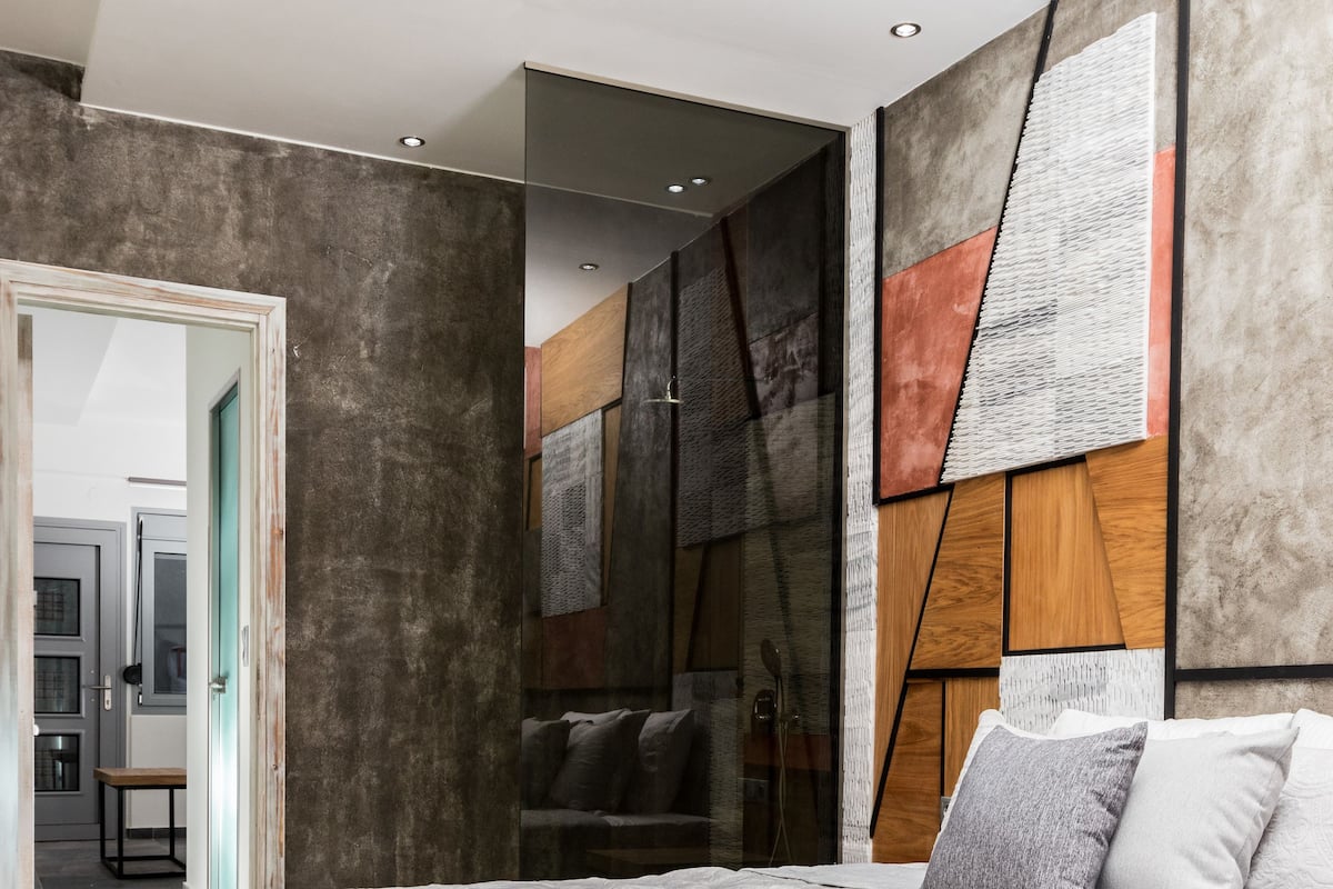 A modern bedroom with a large bed, a wooden headboard, and a view of the adjacent bathroom.