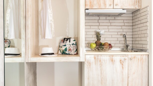 A compact bedroom with a bed, a small kitchenette with a sink and a fruit bowl, and a mirror with a hanging garment. - Lena Apartments (Thasos)