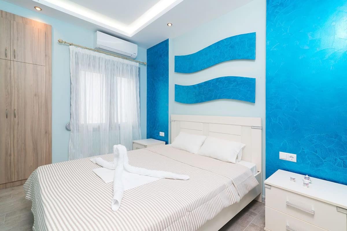 A modern bedroom with a large bed, a wooden wardrobe, a nightstand, and a white dresser.