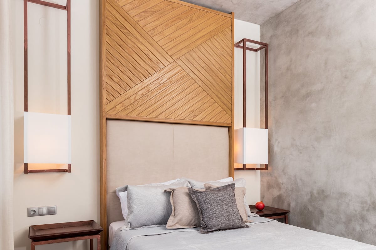 A modern bedroom with a wooden headboard, bedside lamps, and a bedside table.