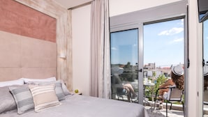 A bedroom with a large bed, a sliding glass door to a balcony, and a view of the city. - Lena Apartments (Thasos)