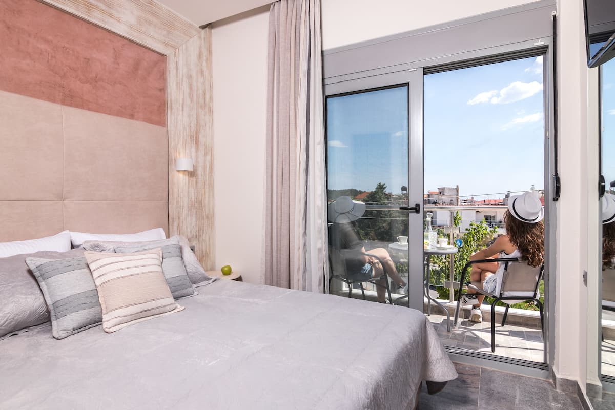 A bedroom with a large bed, a sliding glass door to a balcony, and a view of the city.