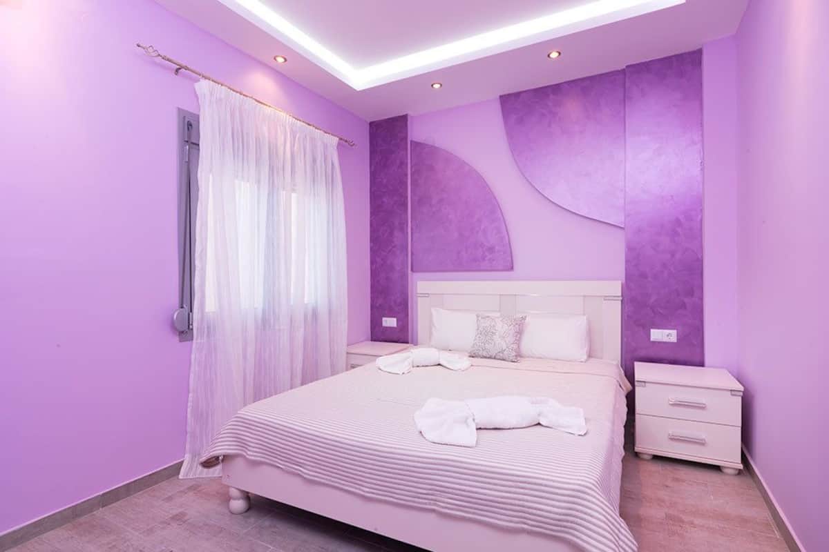 A modern bedroom with a large bed, a nightstand, and a window with sheer curtains.